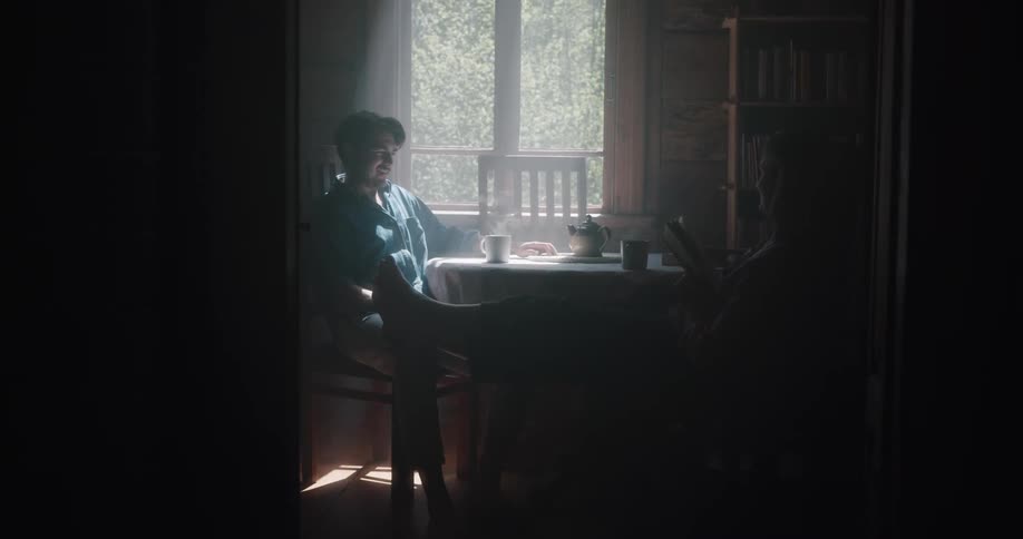 A man brings his wife coffee and joins her in sitting at their kitchen table