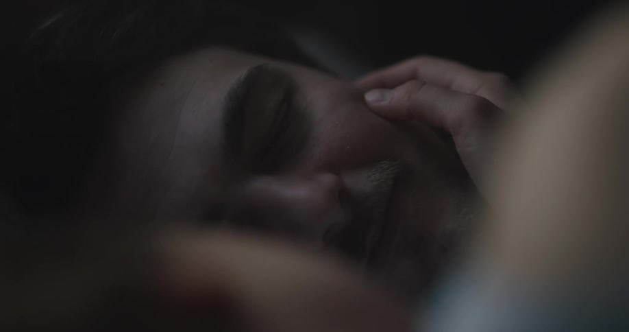 A man and a woman in a bedroom laying on a bed with the woman caressing the mans face