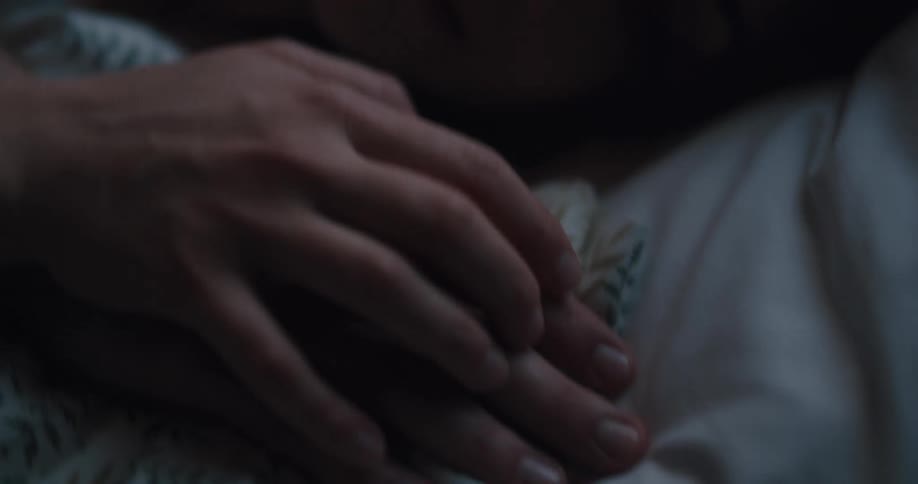 A man spooning his wife caresses her hand with his fingers
