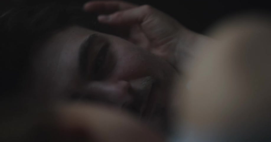 Couple lie down together smiling as one strokes the others hair