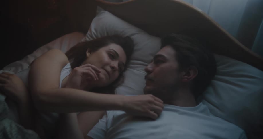 A man and a woman in a bedroom laying in a bed with a pillow