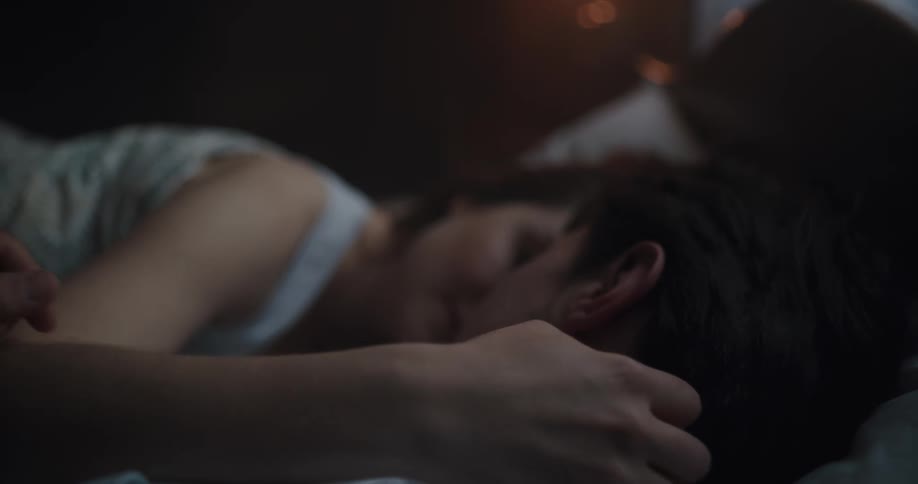 Couple lies on bed cuddling the man stroking the womans arm while she strokes his hair