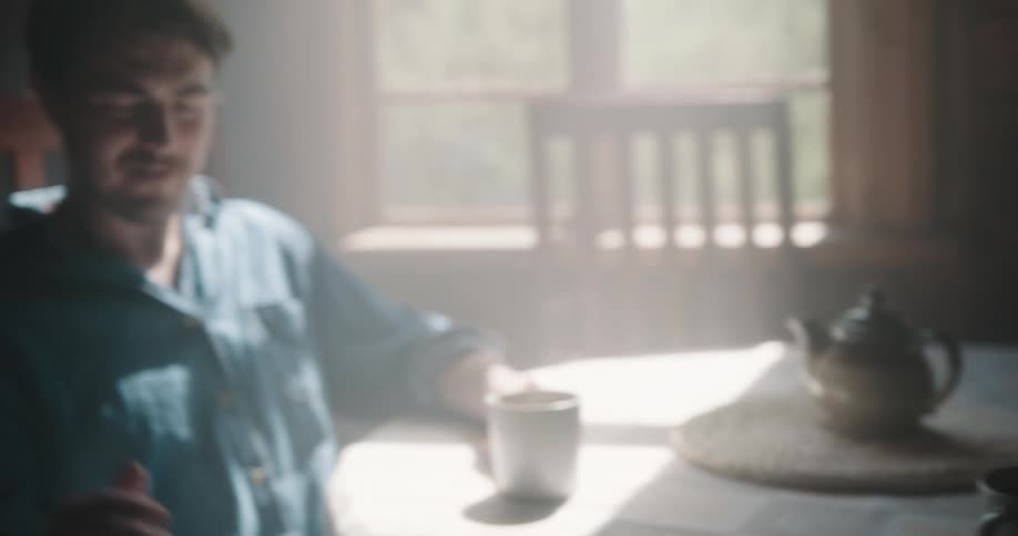 Man walks in and puts coffee on table where woman is sitting reading before joining her to talk and drink his own coffee