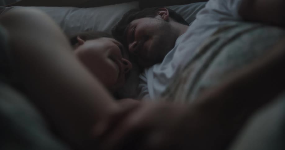 Man and woman lie together in bed smiling and talking
