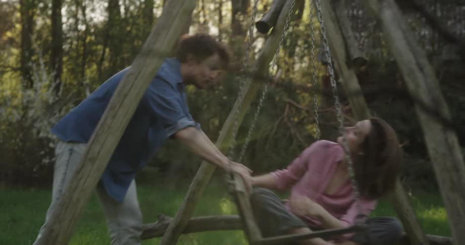 Young couple playing on a wooden swing in near a cabin in the countryside at morning