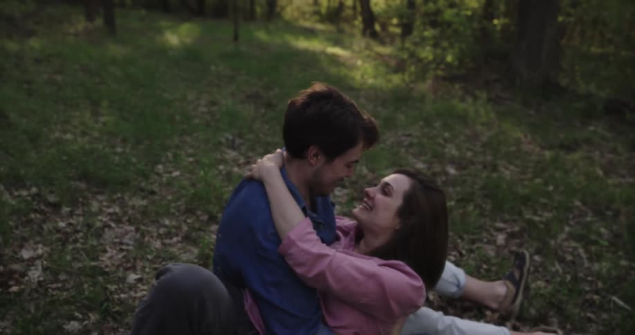 Couple sit on ground in field cuddling and kissing