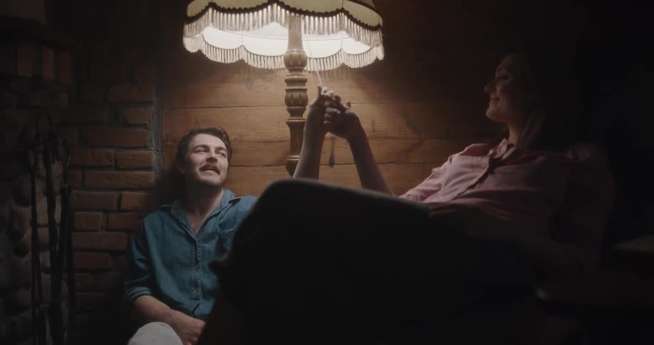 A man and a woman in a room turning on and off a lamp with a wall and fireplace in the background