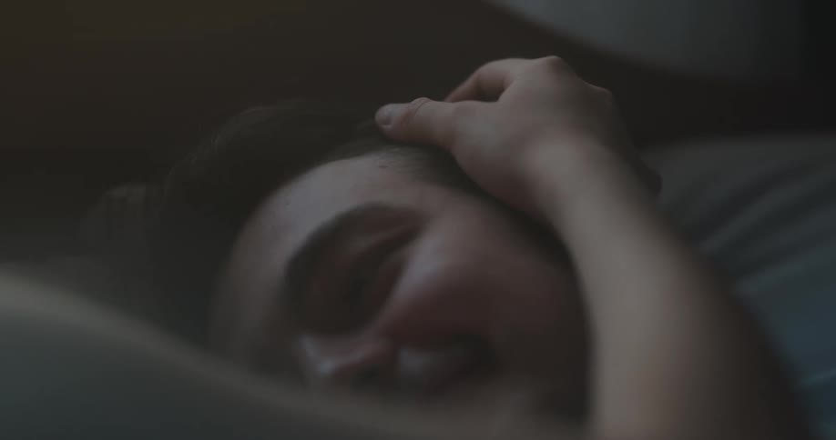 A man smiles as his wife caresses his cheek and plays with his hair while they are in bed