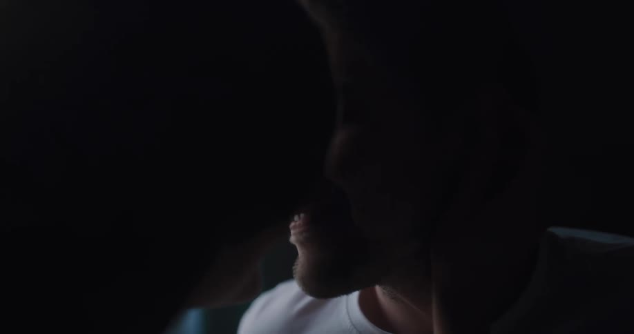 A woman caressing the face of a smiling man with her hand before they share a kiss