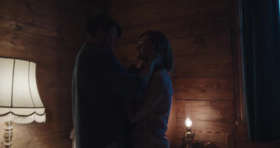 A man and a woman in a room with the woman pushing the man with a wall a lamp and fireplace in the background
