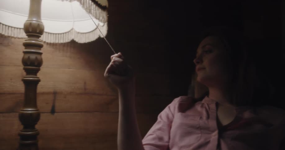 A man and woman sit at home and they both reach for a lamp to turn it off