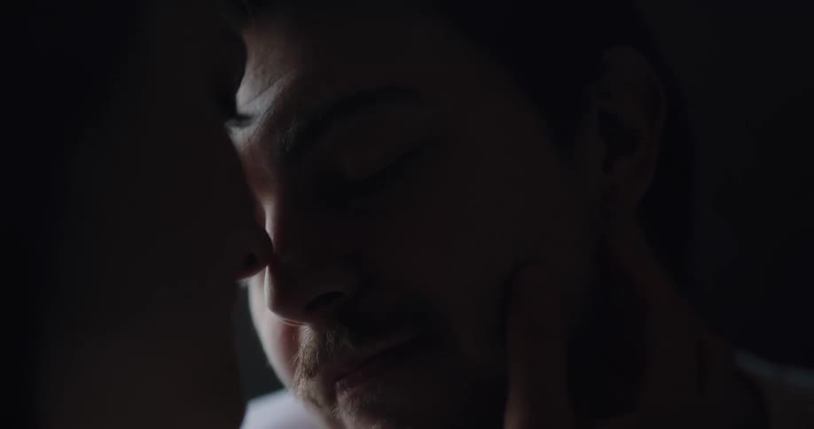 A woman caresses a mans face as they gaze into each others eyes before sharing a kiss