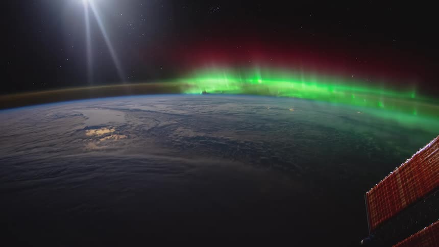 Aurora borealis glows green on horizon contrasting with white and blue of sky and solar panels of station in space under bright light of sun