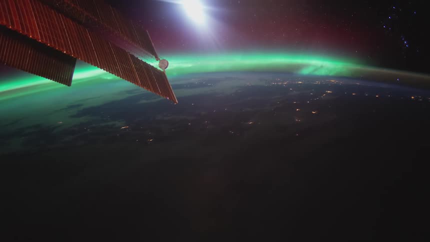 Earth lights shine under green of aurora borealis under space station solar panels