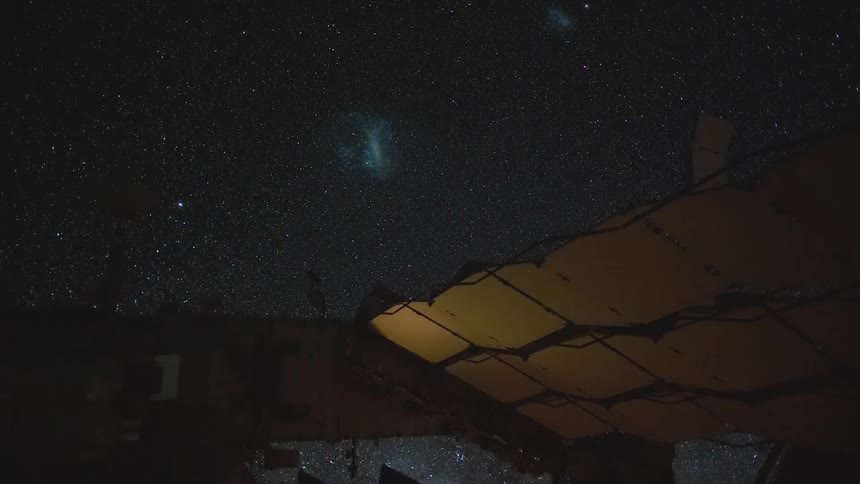 Stars glow against the black of outer space as a satellite floats by