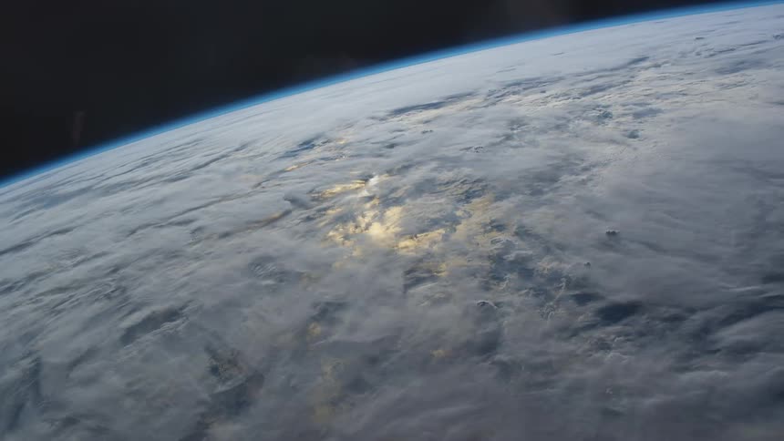 Light glows through the cloud cover on the surface of the earth in space