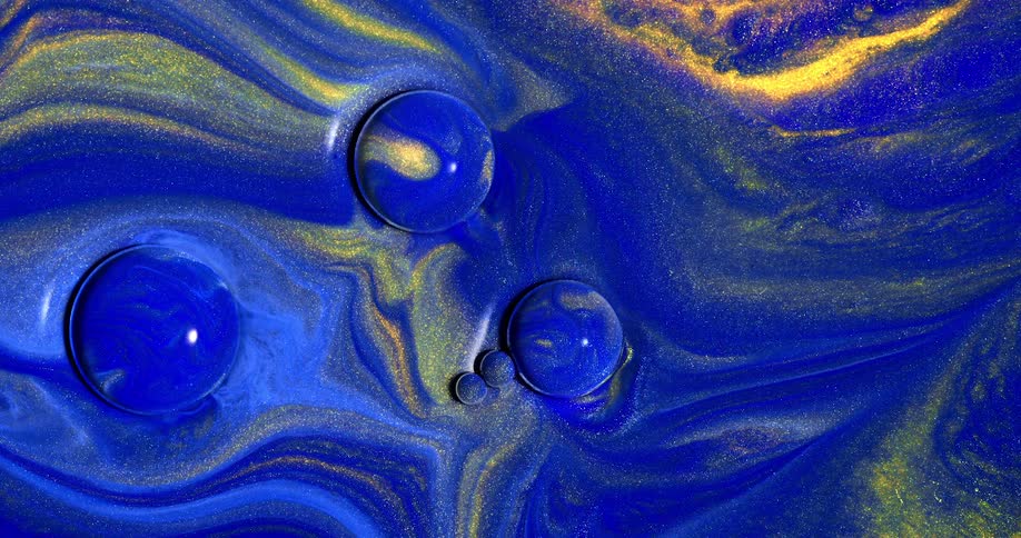 A viscous blue liquid has streaks of blue and yellow in it as there is also glittery material suspended in it