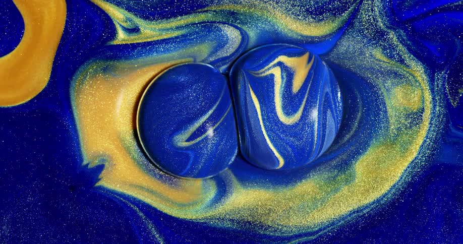 Two globs of liquid paint in blue and yellow crashing into each other