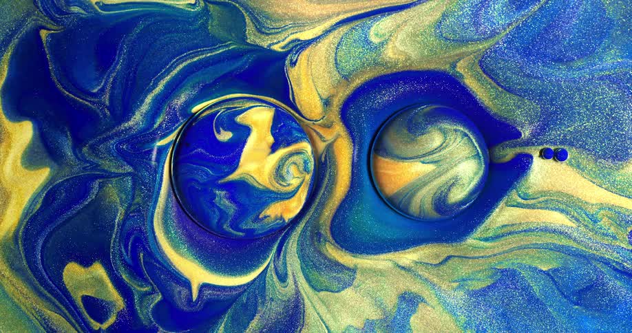 A droplet of a blue and yellow glitter fluid emerges from beneath the liquid surface