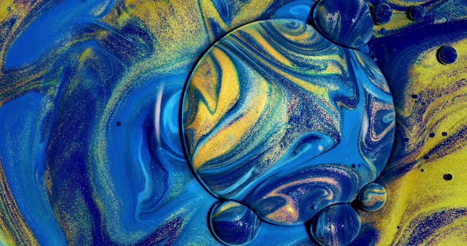 A mixture of blue green and yellow glitter liquids splash and mix together beautifully