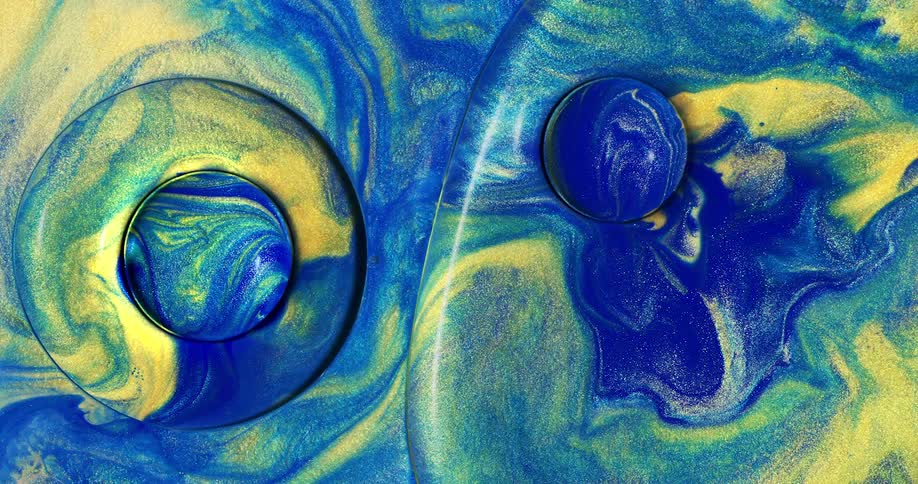 A viscous liquid that is a mixture of glittery blue green and yellow swirls around and mixes together