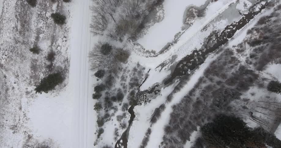 A snow covered area with tire tracks and what looks like a small body of water