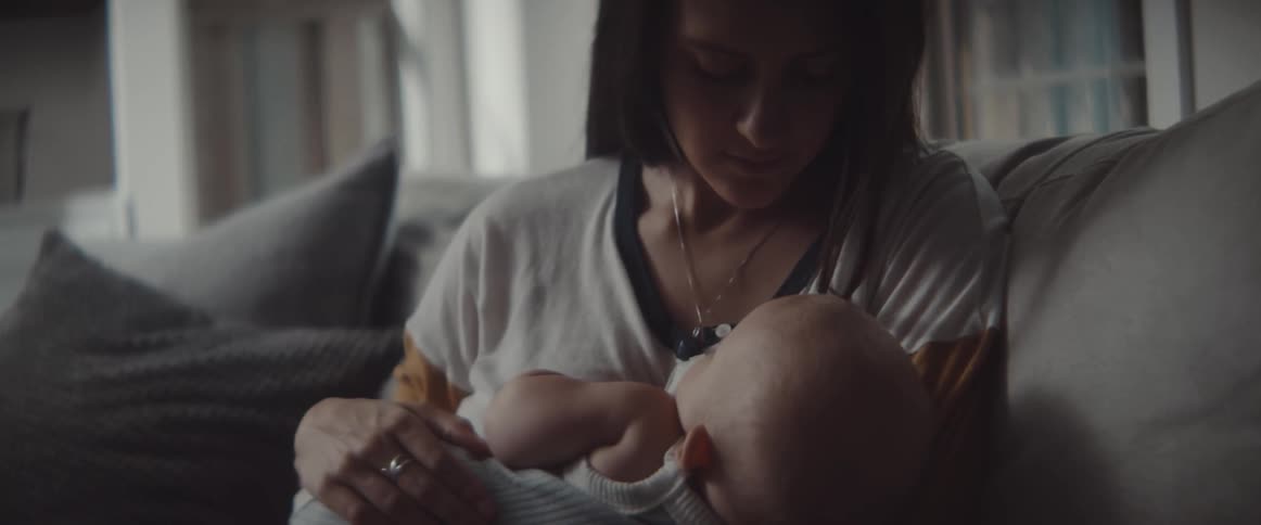 A woman sits on a couch and snuggles with an infant