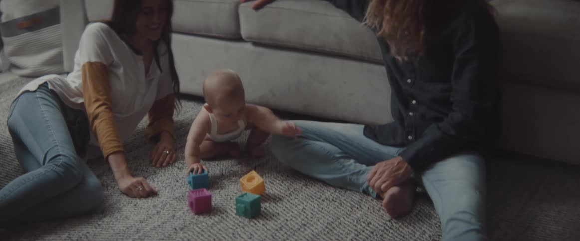 A couple sit on the floor with their infant son as he plays with blocks