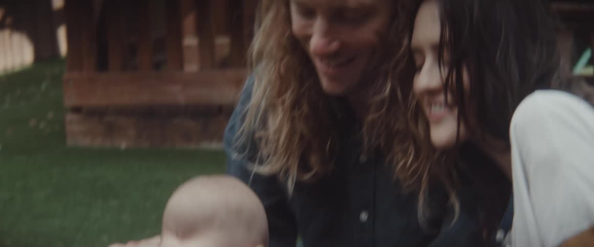 A man and woman kiss as they play outside with their infant son