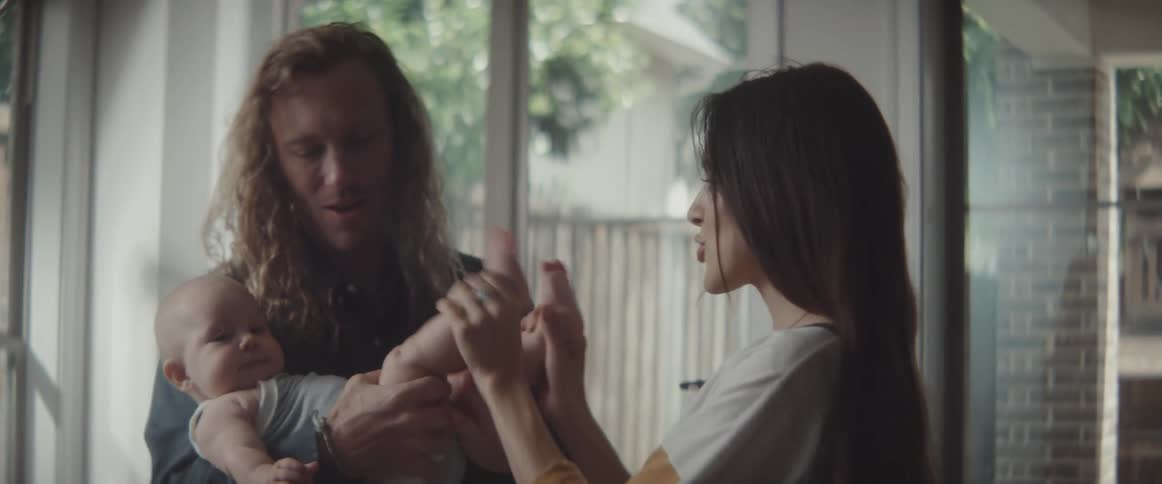 A man and a woman in a room playing with a baby with a door and windows in the background