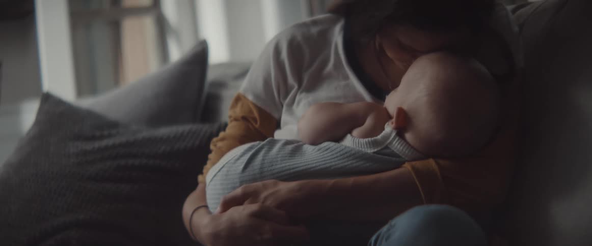 A woman sits on a couch snuggling and kissing a baby