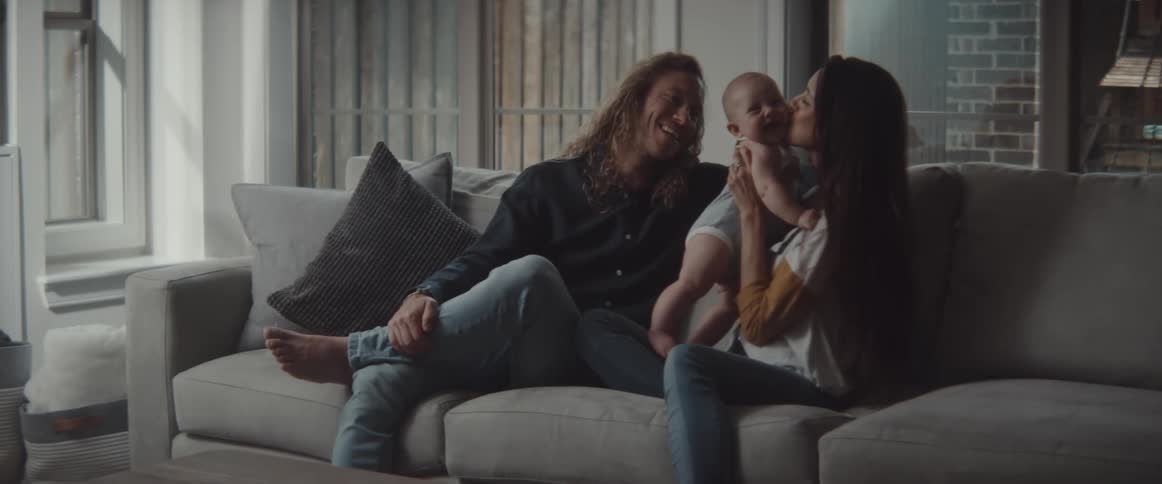 The mother kisses the baby as they sit on the couch
