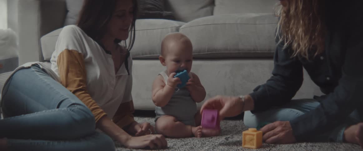 A mom and dad sitting on the living room rug playing with their baby
