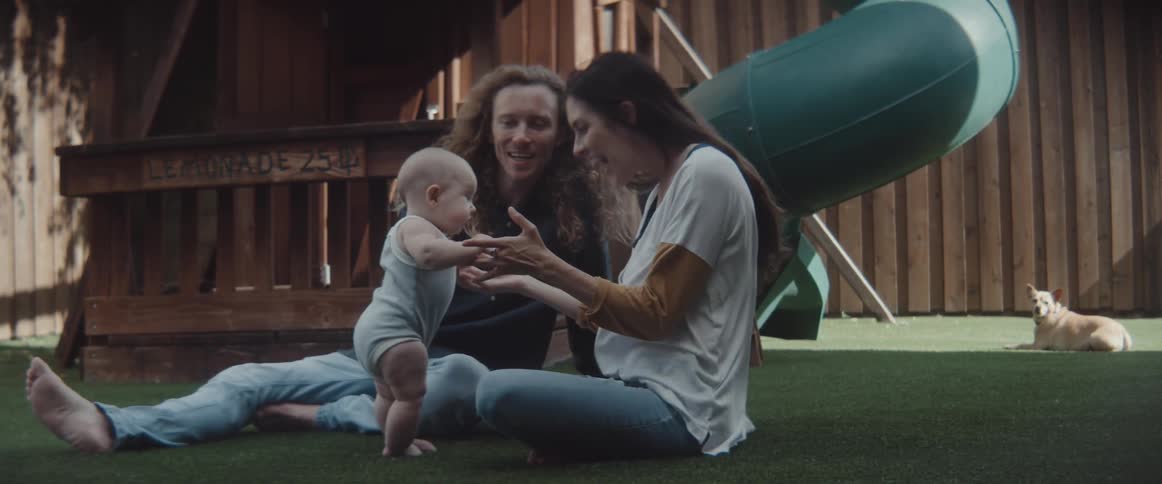 Couple playing with their baby sitting on the ground next to a playground
