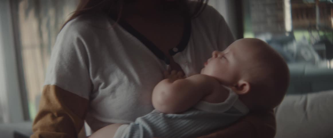 A woman rocks a sleeping baby in her arms while standing in the living room of house during the day