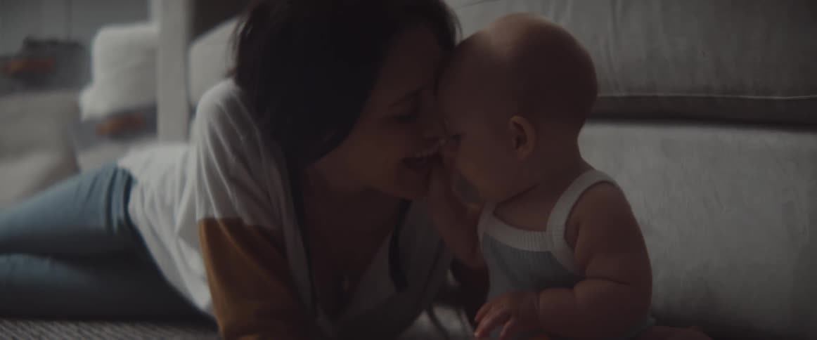 A woman lies on the floor and kisses her baby