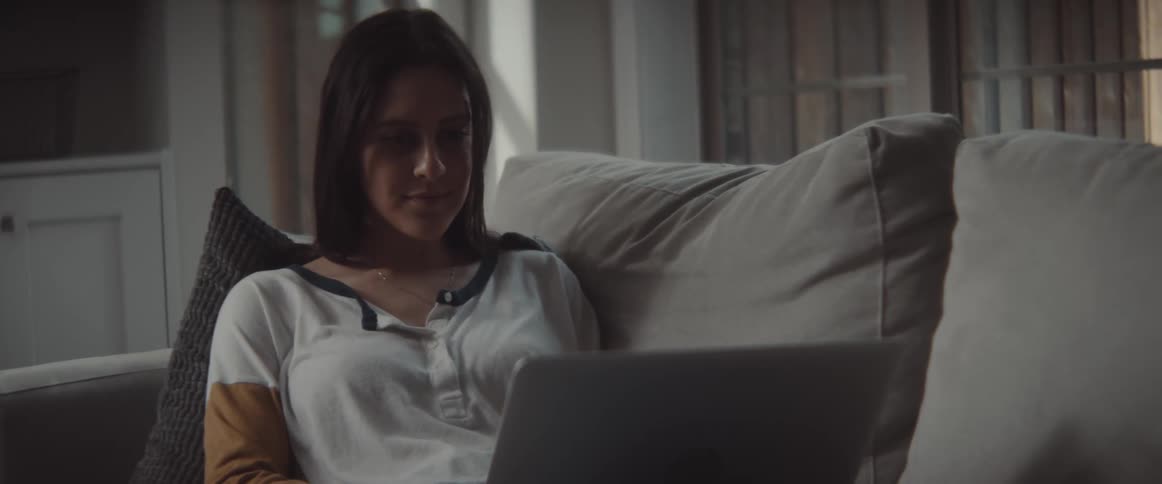 A woman is laying on hte couch typing on the laptop