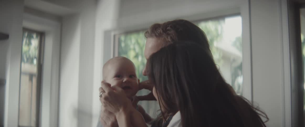 A man lifts a baby in the air while laughing with a woman