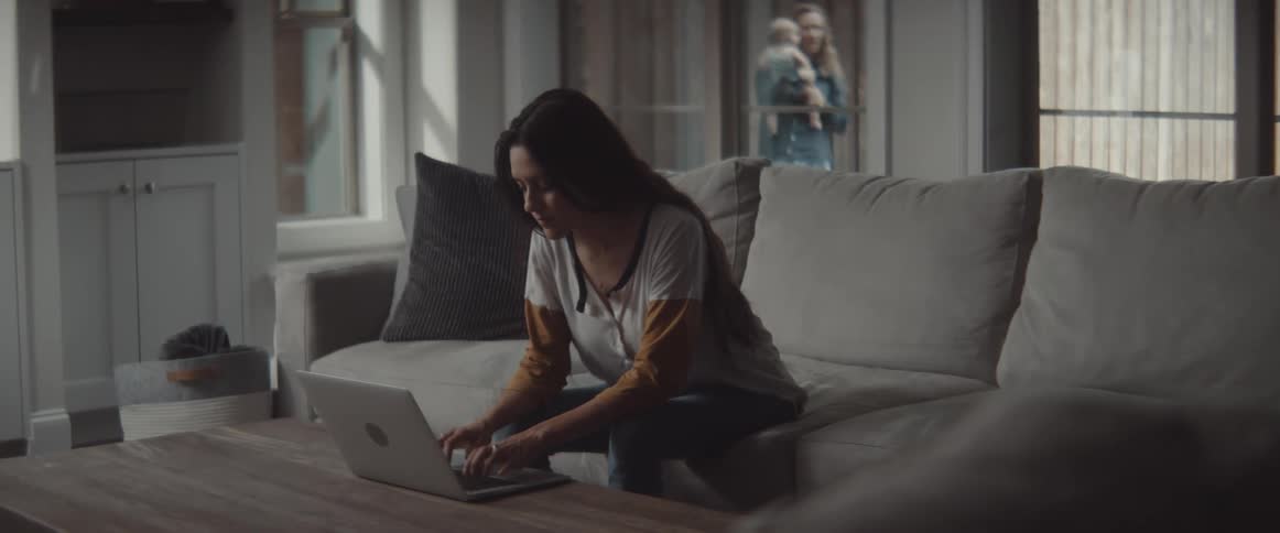 Woman working from home while her husband plays with their son outdoors