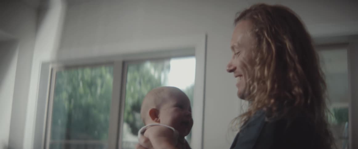 A man raises a baby in the air and laughs