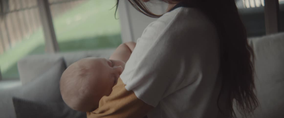 Woman with long dark hair sweatshirt holds baby in the living room at home