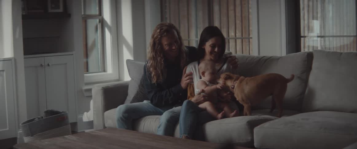 Father with wavy long hair and brunutte mother hold baby and caress small dog in the living room