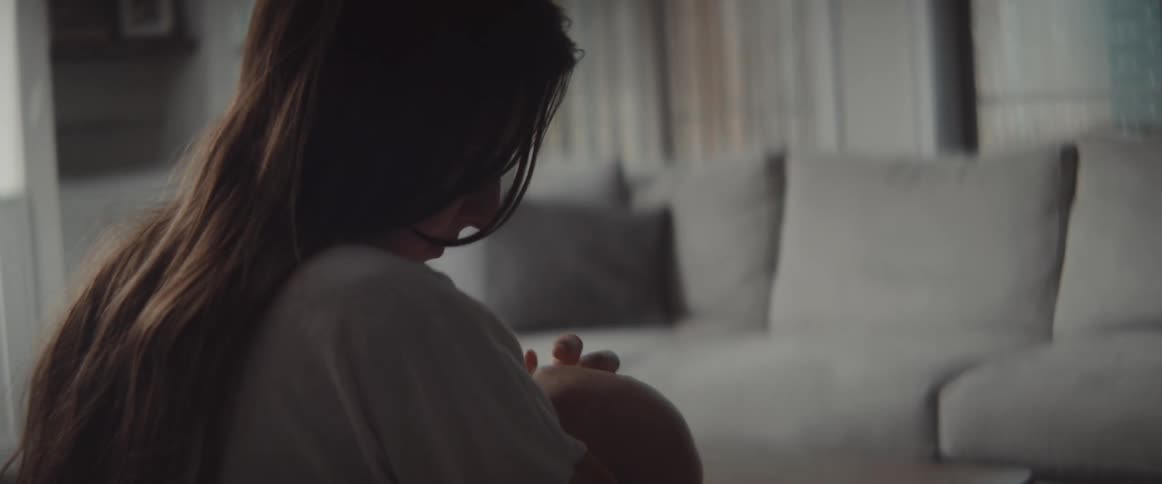 A woman in a room holding a baby with a table and a couch in the background