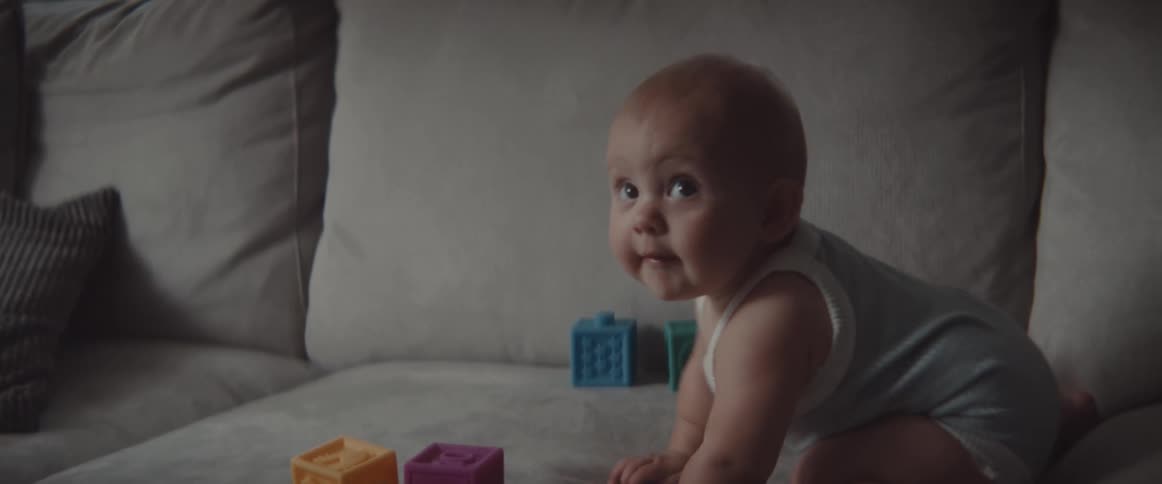 Happy baby playing with colorful plastic blocks over a couch at home