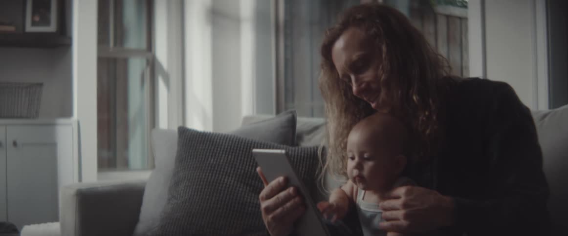 A man and a baby in a room sitting on a couch looking at a tablet
