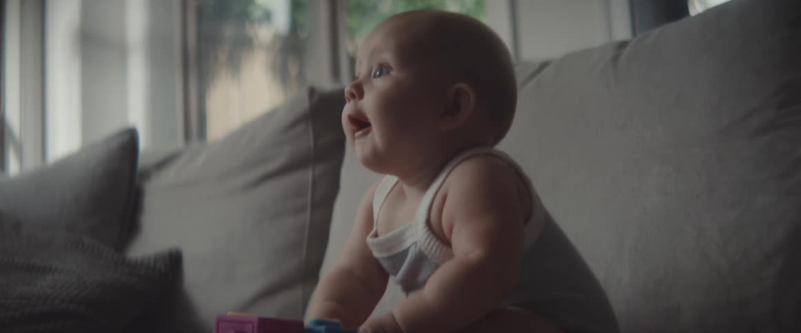 A baby holds a toy block while sitting on a sofa in the living room of a house during the day