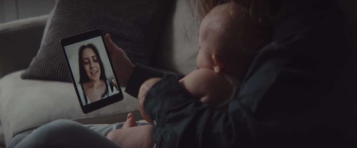 A man in a room sitting on a couch holding a baby and a tablet