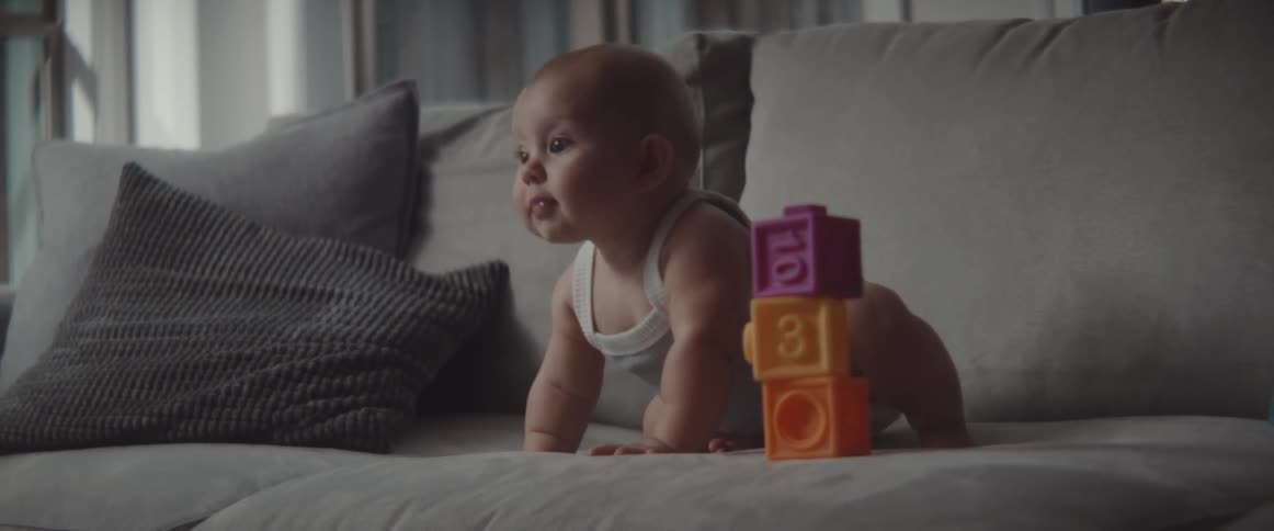A baby is on the couch playing with blocks