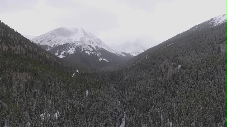 Aerial view of a mountain valley and snow-capped mountains as it snows