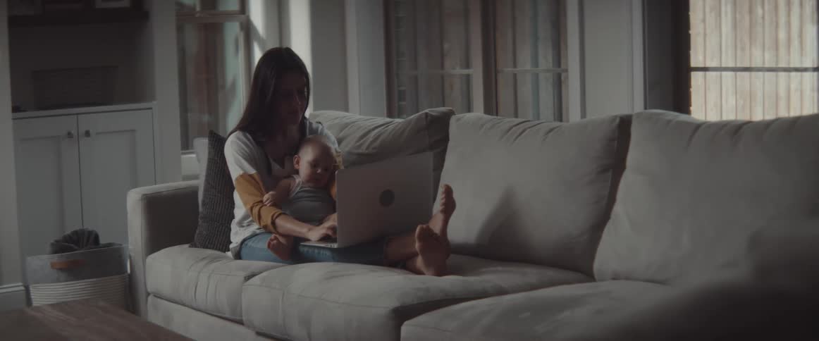 Mother holding son in her lap typing on a laptop over a couch on the living room